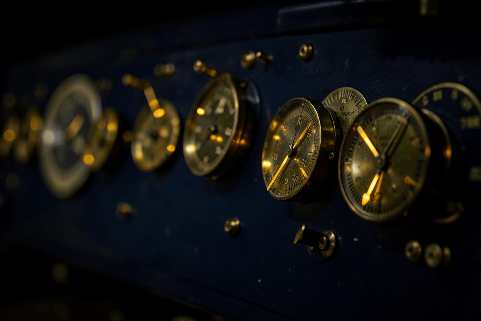 A row of brass gauges with glowing gold needles on a deep navy panel